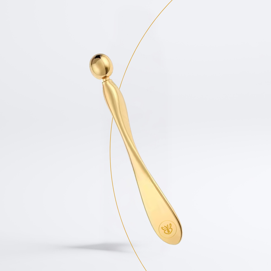 Vue rapprochée du masseur oculaire doré posé sur fond beige clair, accessoire beauté chic